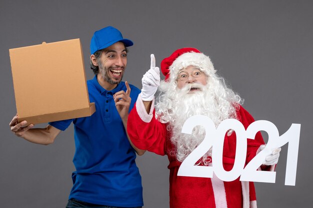 Front view of santa claus with male courier holding food box and on a grey wall