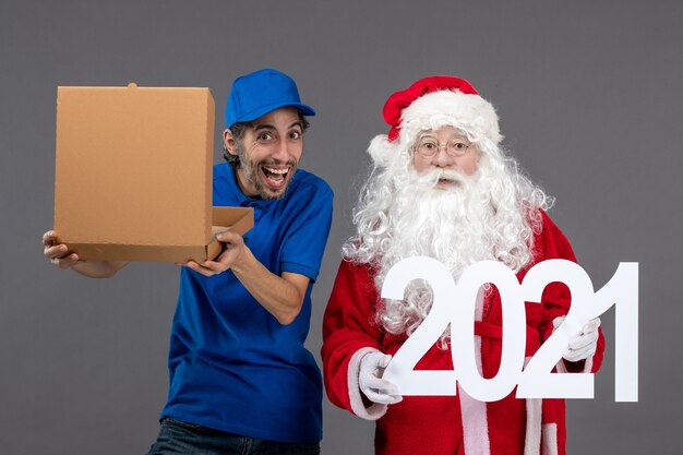 Front view of santa claus with male courier holding food box and writing on grey wall