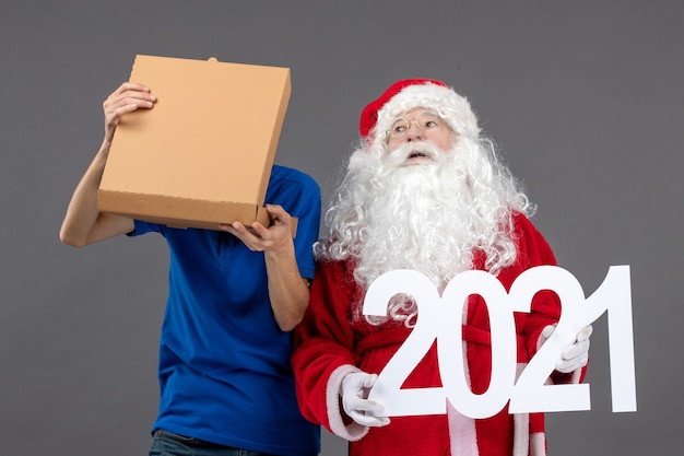 Free photo front view of santa claus with male courier holding food box and writing on grey wall