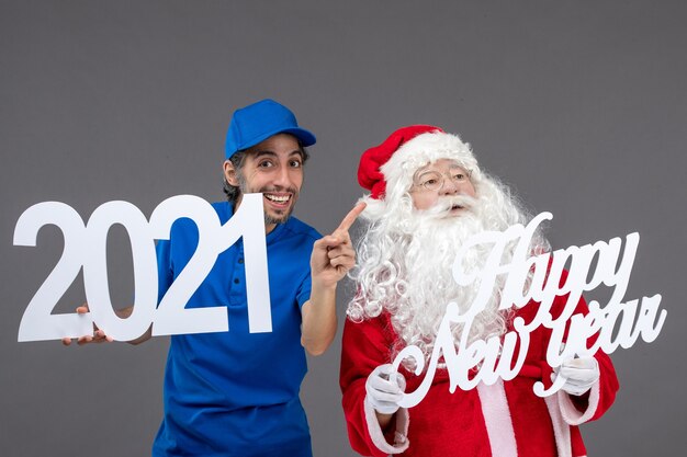 Front view of santa claus with male courier holding and happy new year and 2021 boards on a grey wall