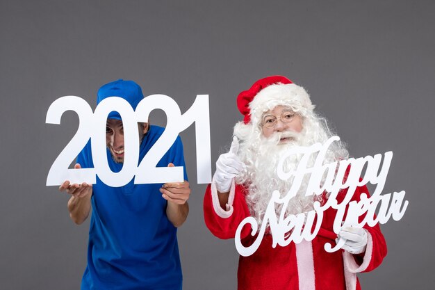 Front view of santa claus with male courier holding and happy new year and 2021 boards on a grey wall