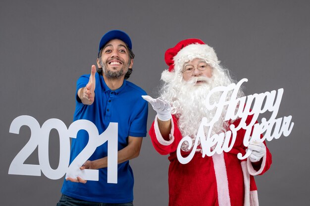 Front view of santa claus with male courier holding and happy new year and 2021 boards on grey wall