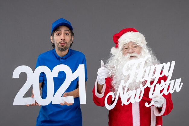 Front view of santa claus with male courier holding and happy new year and 2021 boards on grey wall