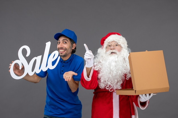 Front view of santa claus with male courier holding sale banner and food box on the grey wall