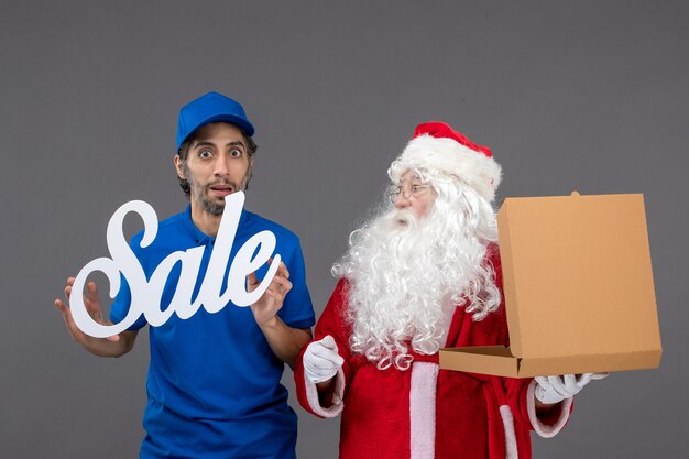 Front view of santa claus with male courier holding sale banner and food boxes on a grey wall