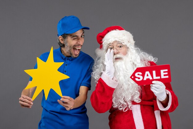 Front view of santa claus with male courier holding sale banner and yellow sign on grey wall