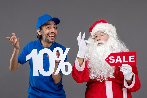 Front view of santa claus with male courier holding sale banners on a grey wall