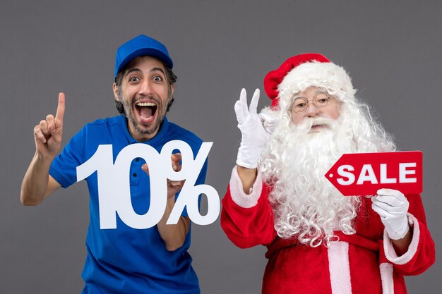 Front view of santa claus with male courier holding sale banners on grey wall