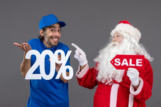 Front view of santa claus with male courier holding sale banners on a grey wall