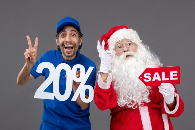 Front view of santa claus with male courier holding sale banners on a grey wall