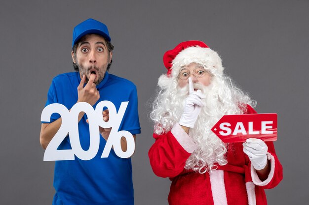 Front view of santa claus with male courier holding sale banners on a grey wall