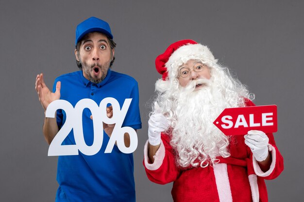 Front view of santa claus with male courier holding sale banners on grey wall