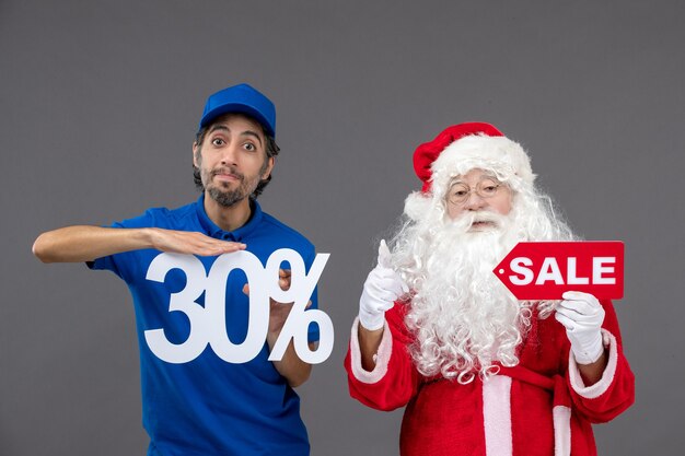 Front view of santa claus with male courier holding sale banners on grey wall