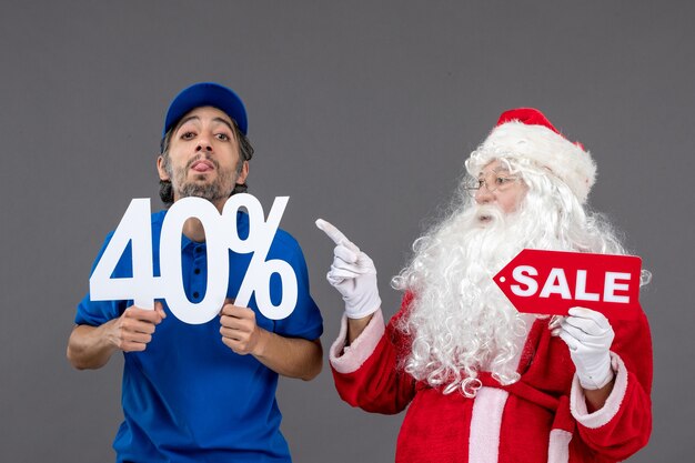 Front view of santa claus with male courier holding sale banners on a grey wall