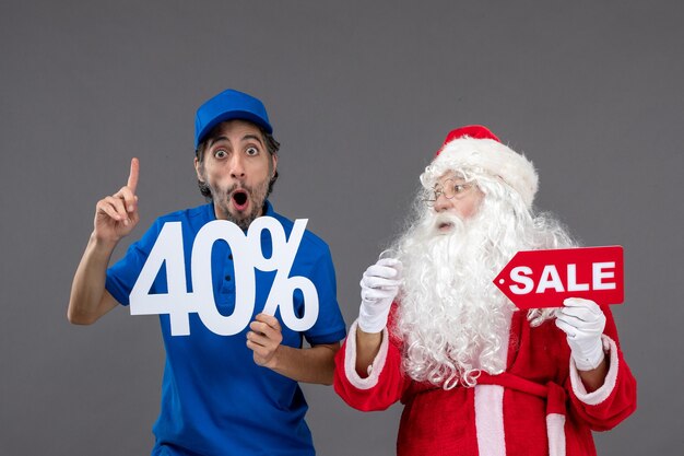 Front view of santa claus with male courier holding sale banners on grey wall