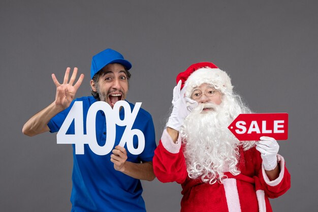 Front view of santa claus with male courier holding sale banners on grey wall