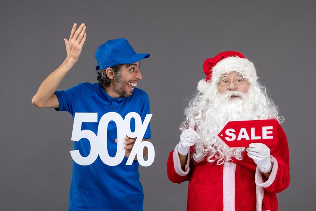 Front view of santa claus with male courier holding sale banners on the grey wall