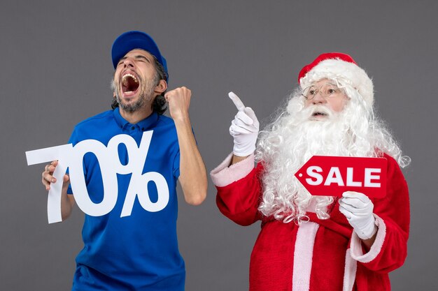 Front view of santa claus with male courier holding sale banners on a grey wall