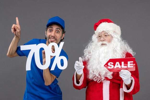 Front view of santa claus with male courier holding sale banners on grey wall