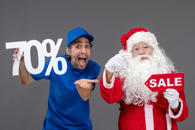 Front view of santa claus with male courier holding sale banners on grey wall