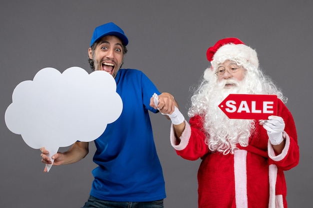 Front view of santa claus with male courier holding sale writing and cloud sign on grey wall