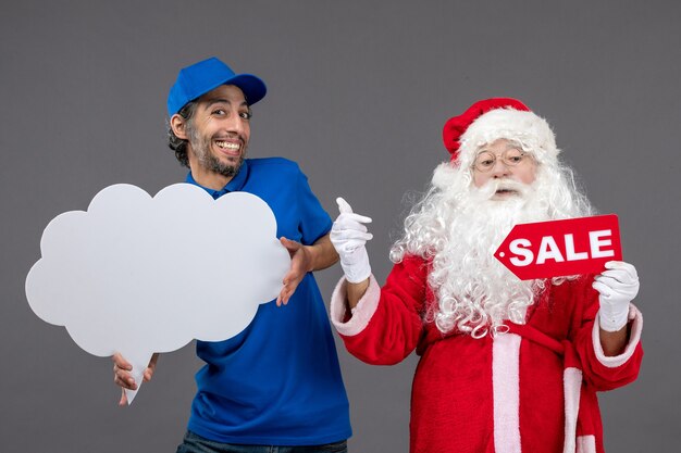 Front view of santa claus with male courier holding sale writing and cloud sign on grey wall