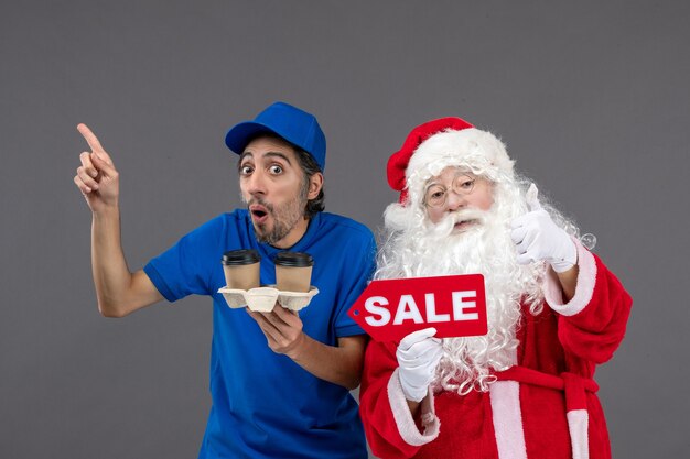 Front view of santa claus with male courier holding sale writing and coffee on a grey wall