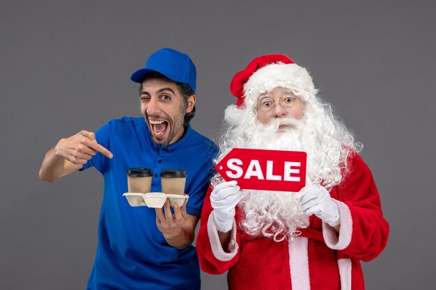 Front view of santa claus with male courier holding sale writing and coffee on a grey wall