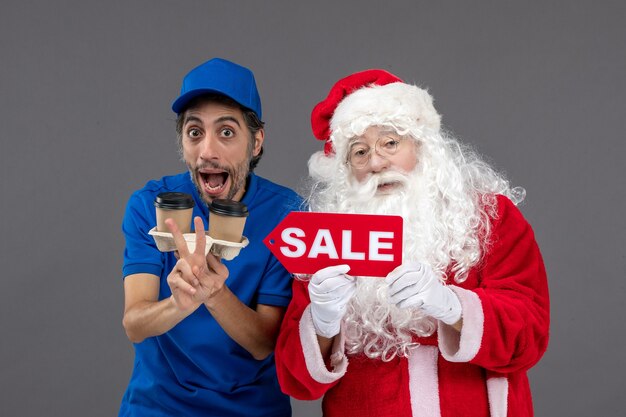 Front view of santa claus with male courier holding sale writing and coffee on grey wall