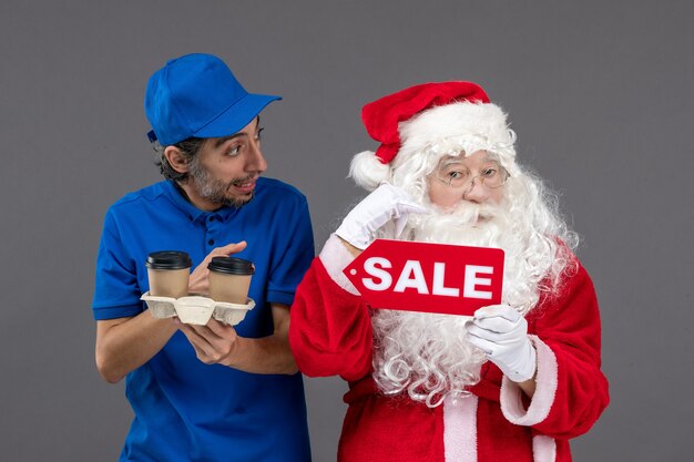 Front view of santa claus with male courier holding sale writing and coffee on grey wall