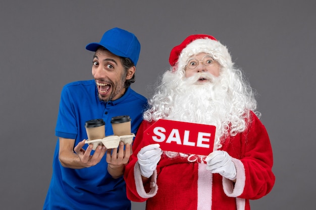 Front view of santa claus with male courier holding sale writing and coffee on grey wall