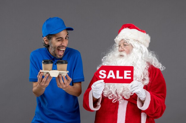 Front view of santa claus with male courier holding sale writing and coffee on grey wall