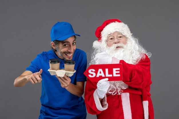 Front view of santa claus with male courier holding sale writing and coffee on grey wall