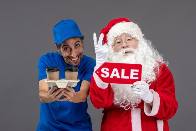 Front view of santa claus with male courier holding sale writing and coffee on the grey wall