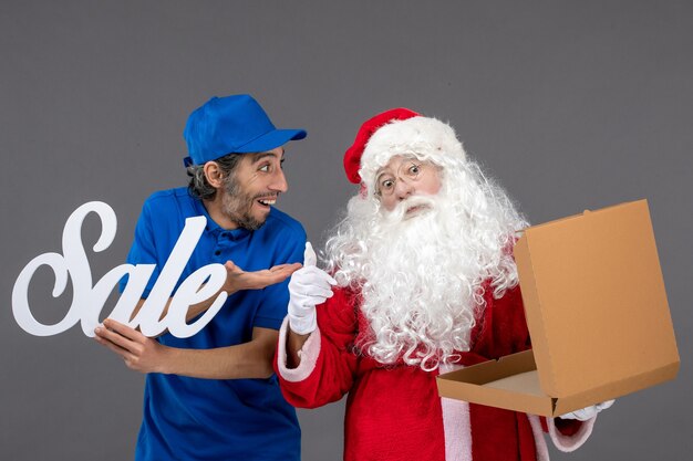 Front view of santa claus with male courier holding sale writing and empty food box on grey wall