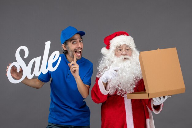 Front view of santa claus with male courier holding sale writing and food box on grey wall