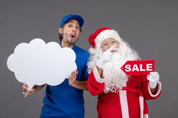 Front view of santa claus with male courier holding white cloud sign and sale on grey wall