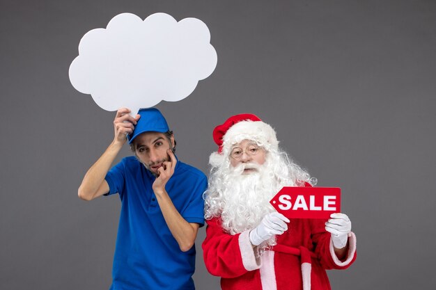 Front view of santa claus with male courier holding white cloud sign and sale on grey wall