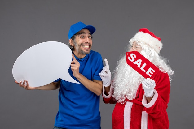 Front view of santa claus with male courier holding white sign and sale banner on grey wall