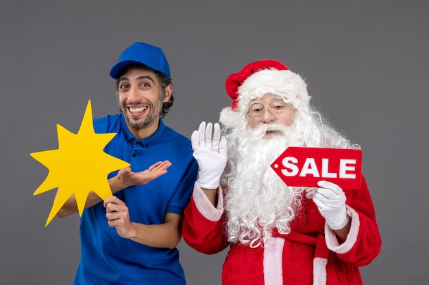 Front view of santa claus with male courier holding yellow sign and sale banner on the grey wall