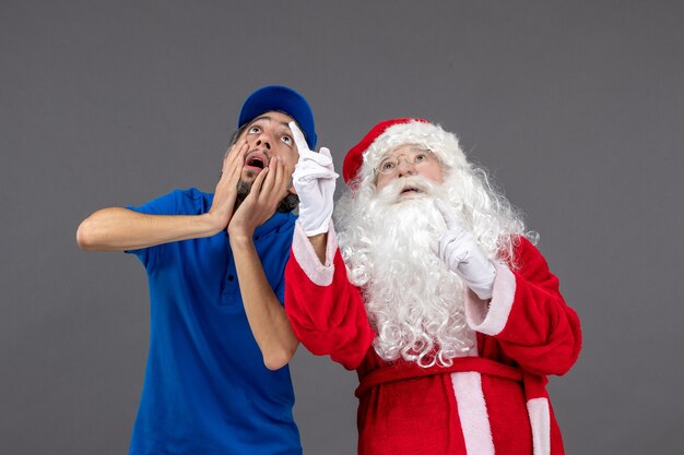 Front view of santa claus with male courier looking at sky on grey wall