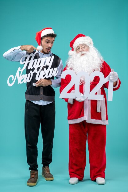 Front view of santa claus with male holding happy new year and 2021 boards on blue wall