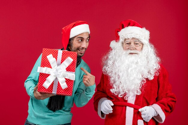 Вид спереди санта-клауса с мужчиной, держащим праздничный подарок на красных эмоциях, красных подарках, рождество, новый год