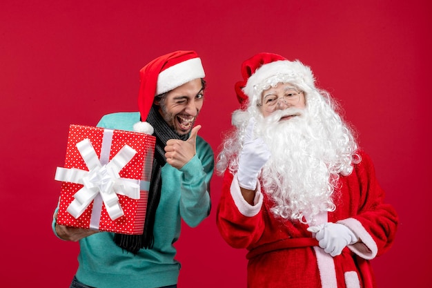 赤い床の感情の赤いギフトクリスマスに休日のプレゼントを保持している男性と正面のサンタクロース