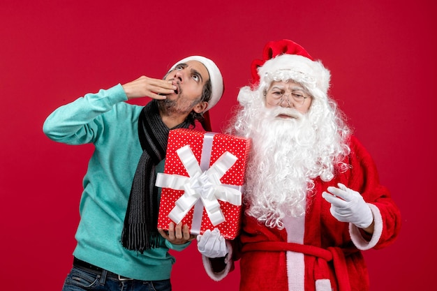 Front view santa claus with male holding holiday present on red gift emotion christmas new year red