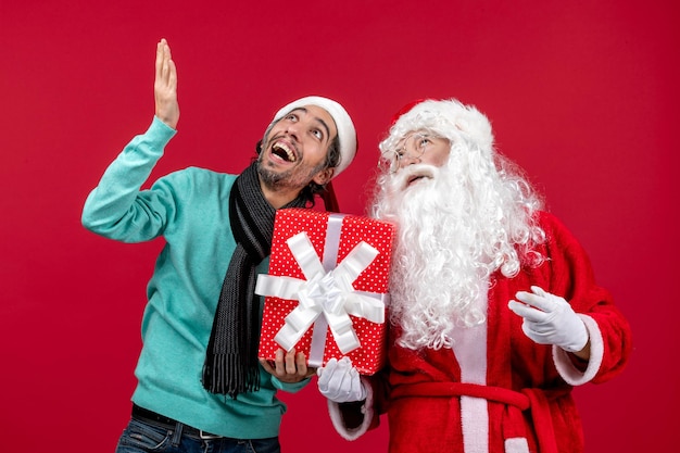 Free photo front view santa claus with male holding holiday present on red gift emotions red christmas new year