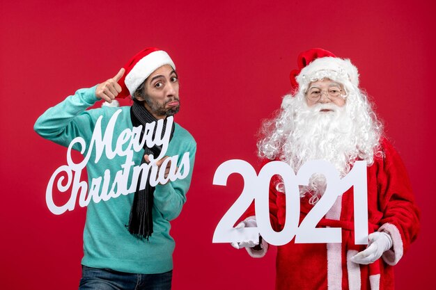 Vista frontale babbo natale con tenuta maschile e scritte di buon natale su colore rosso natale