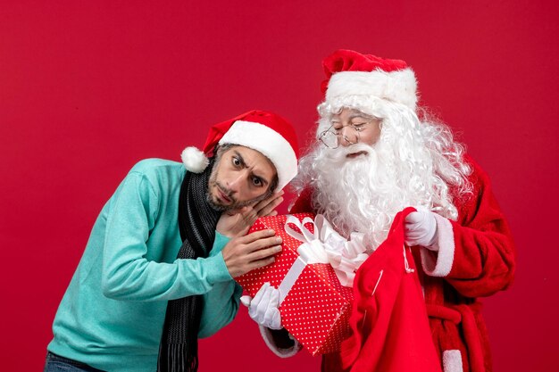 빨간색 크리스마스 감정 새해 휴일 색상에 가방에서 선물을 들고 있는 남성이 있는 전면 보기 산타클로스