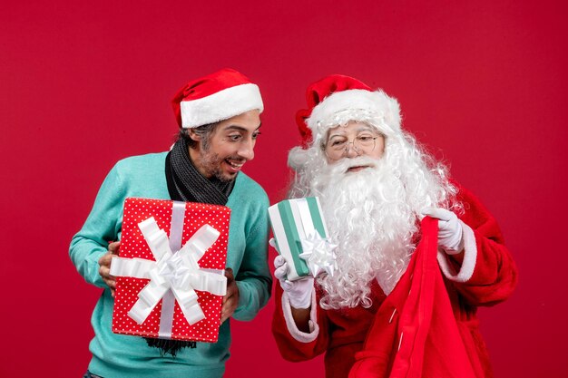 Вид спереди санта-клауса с мужчиной, вынимающим подарки из сумки на красном подарке рождественские эмоции красный