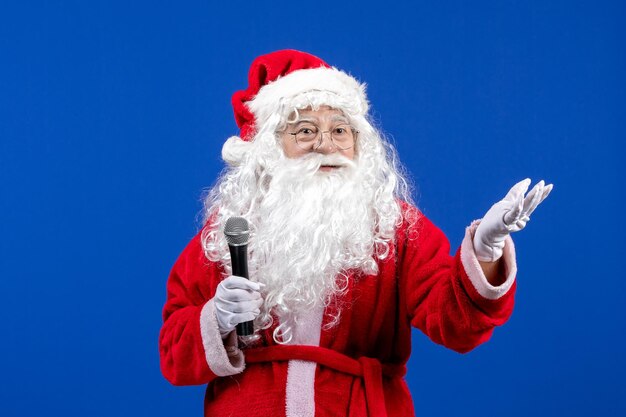 Front view santa claus with red suit and white beard holding mic on a blue color new year holiday
